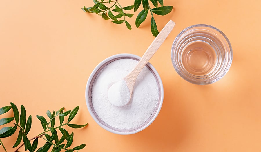 Collagen supplement powder, wooden spoon, and glass of water on orange background