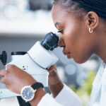 Woman looking into a microscope in a medical lab setting.