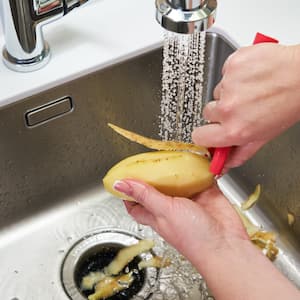 Hands peeling a potato over a garbage disposal while water runs from the faucet