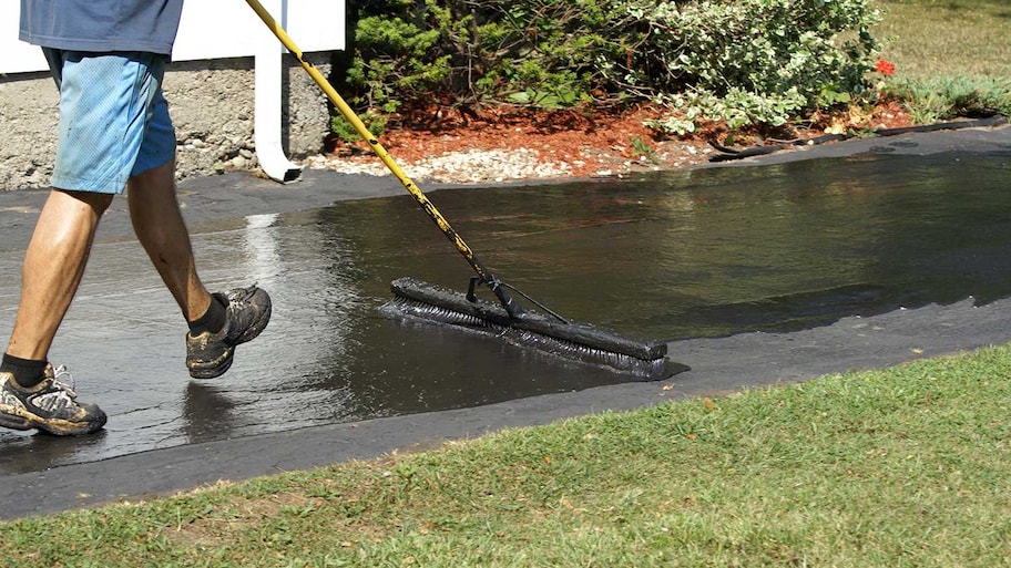 Person sealing asphalt driveway of home