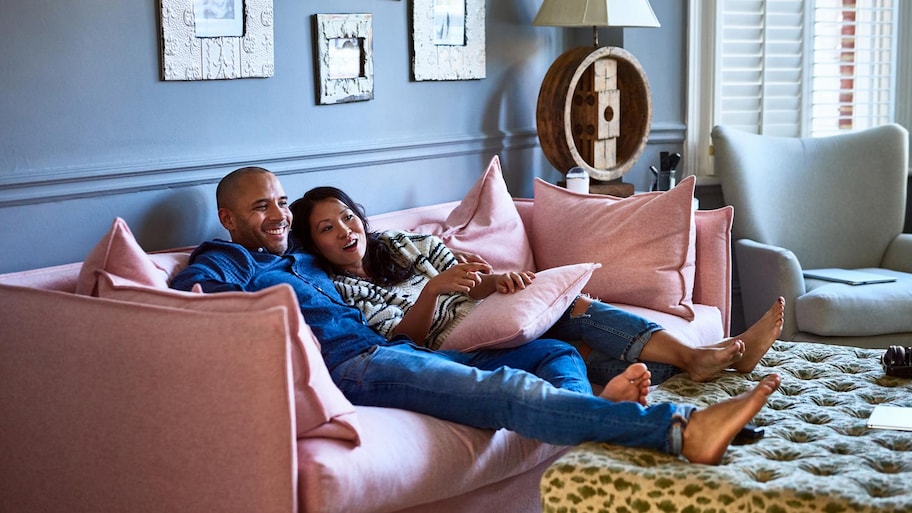 A young couple sitting on a pink sofa and watching tv