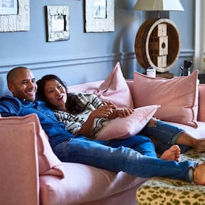 A young couple sitting on a pink sofa and watching tv