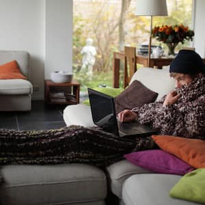 A young man under a blanket working on his laptop