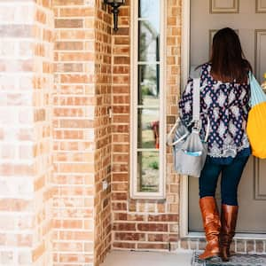 A woman holding flowers entering a brick house