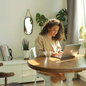 A young woman surrounded by plants using her laptop in her house 