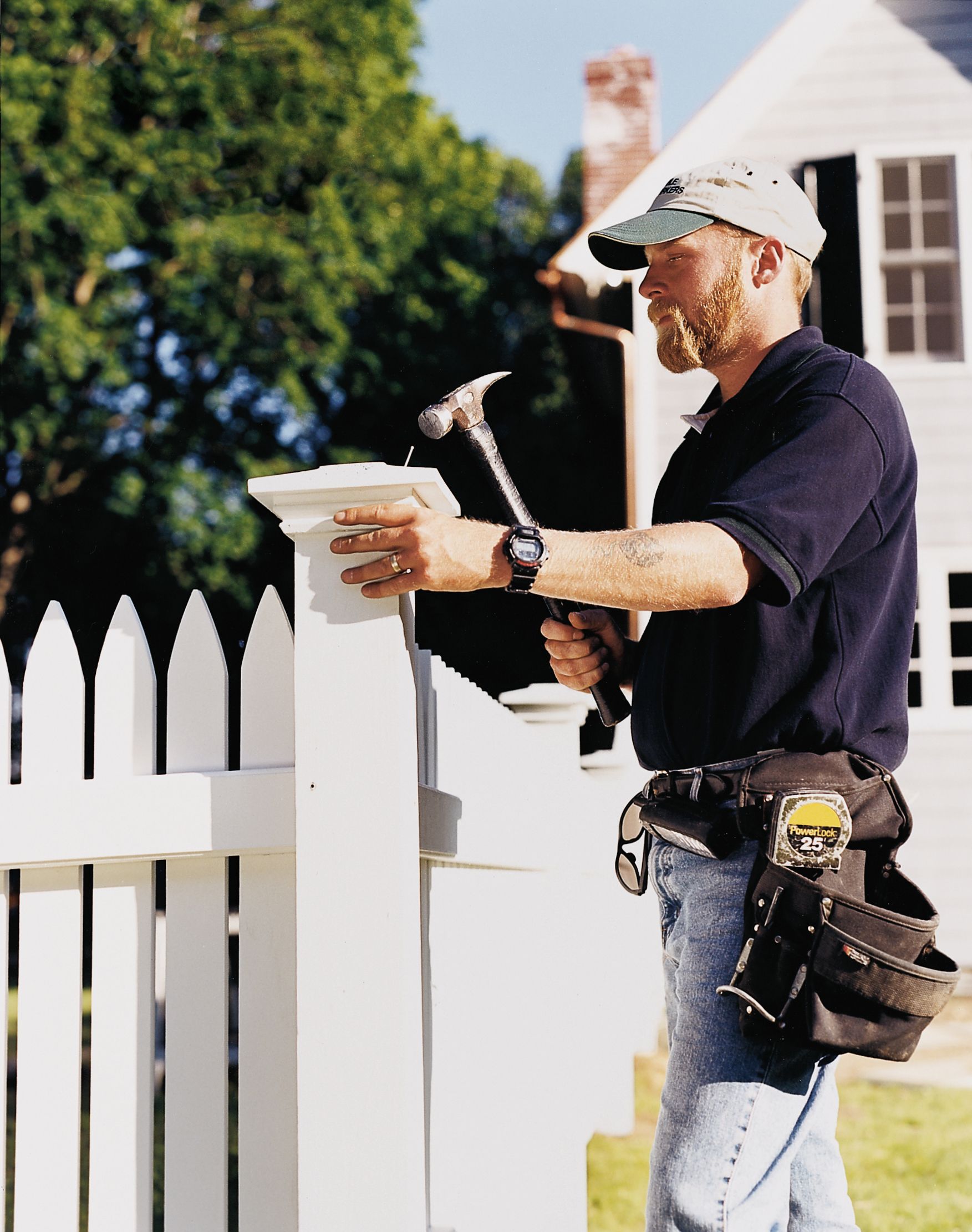 A man using a hammer to install the post of a picket fence.