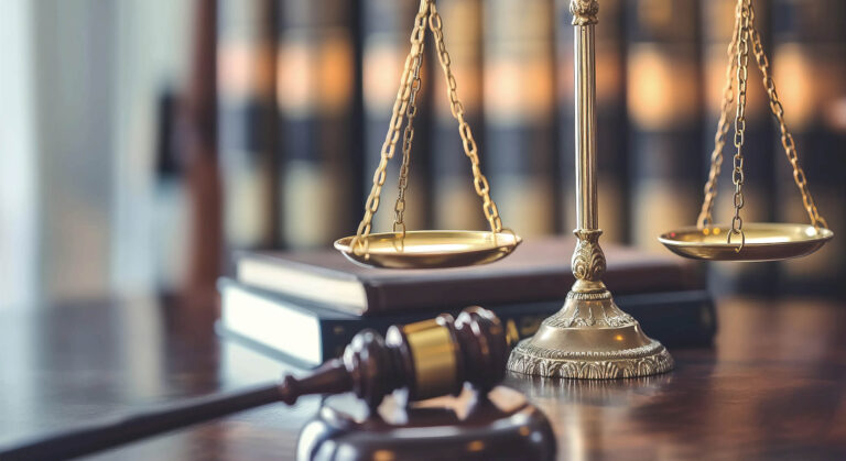 Gavel on a wooden table, placed in front of a brass scale.