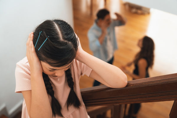 Menina tampando os ouvidos enquanto os pais discutem, uma forma de violência doméstica.