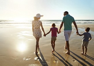 Family walking hand in hand down a Florida beach, wearing bright colors and enjoying their time together.