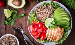 Healthy salad plate with quinoa, cherry tomatoes, chicken, avocado, lime and mixed greens, lettuce, parsley on wooden background