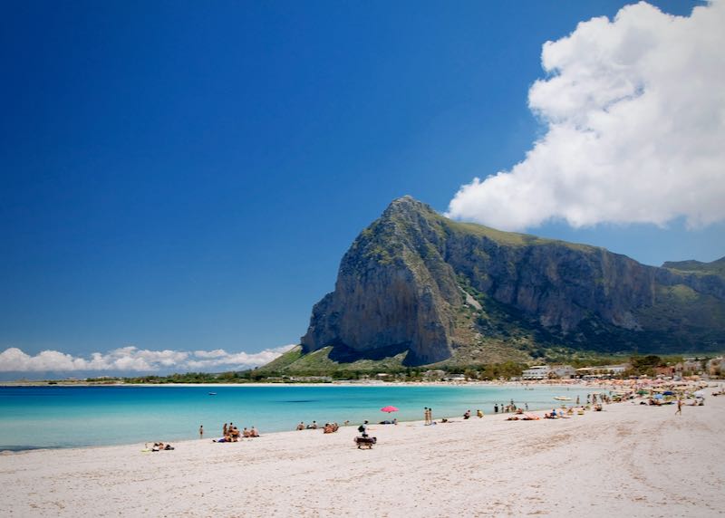 long, white-sand beach, backed by a large rock and rustic buildings