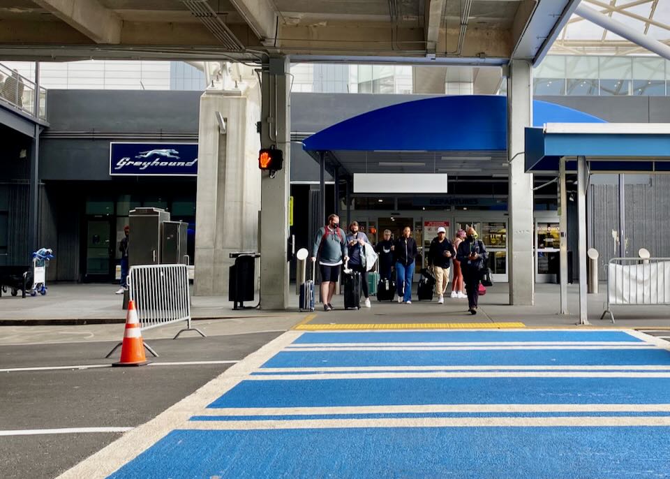 People are waiting to walk the blue crosswalk to the Greyhound airport station.