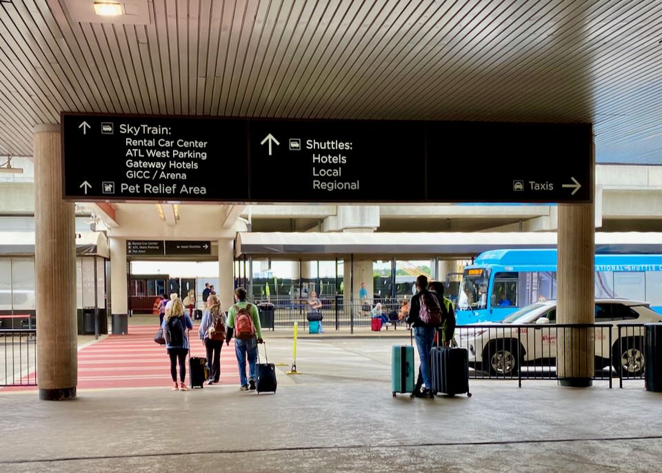 Outside the airport, an overhead sign points north to the shuttles as people walk over the red crosswalk.