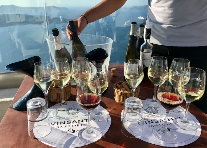 A man serves a flight of white wine on a balcony overlooking the sea