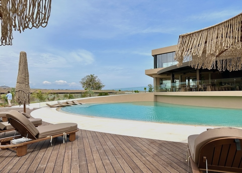 A semicircle pool with a wooden deck and macrame umbrellas with at Pnoe Breathing Life resort in Crete