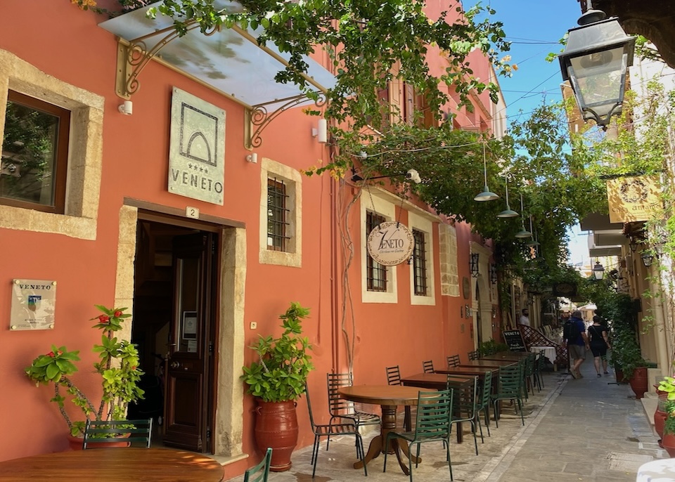 Terra cotta color exterior of Veneto Boutique Hotel with tables set up on the sidewalk and a canopy of vines overhead