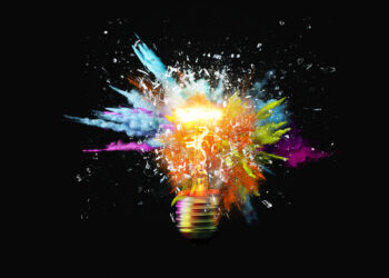 light bulb explodes with colorful paint splashes and shards of glass on a black background