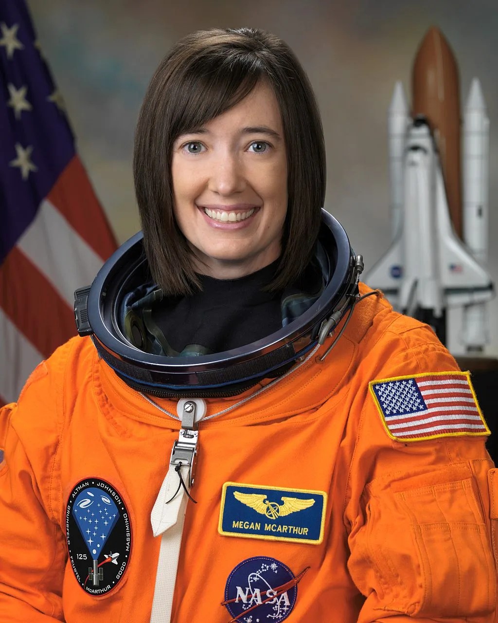 Photo of astronaut Megan McArthur in her orange spacesuit. American flag is behind her.