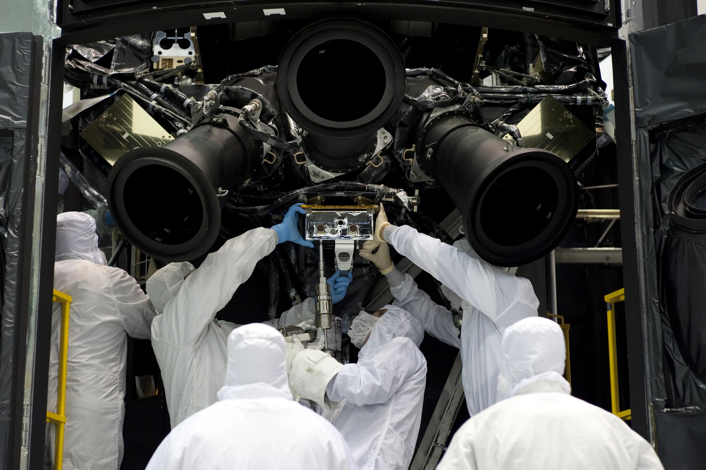 Six people in white clean suits work on the underside of a replica of Hubble.