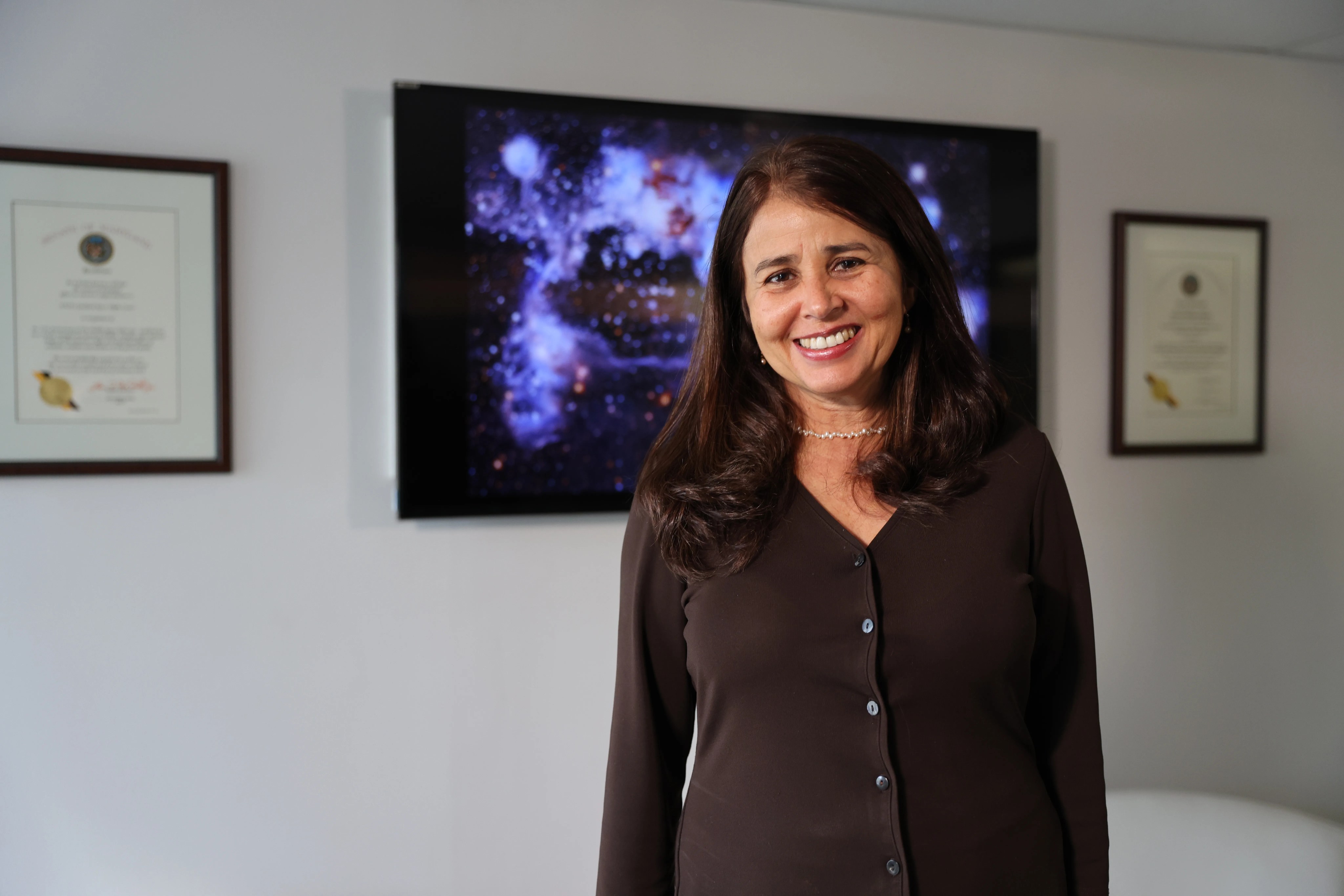 headshot of a woman in dark brown sweater and brown hair standing in front of a Hubble image