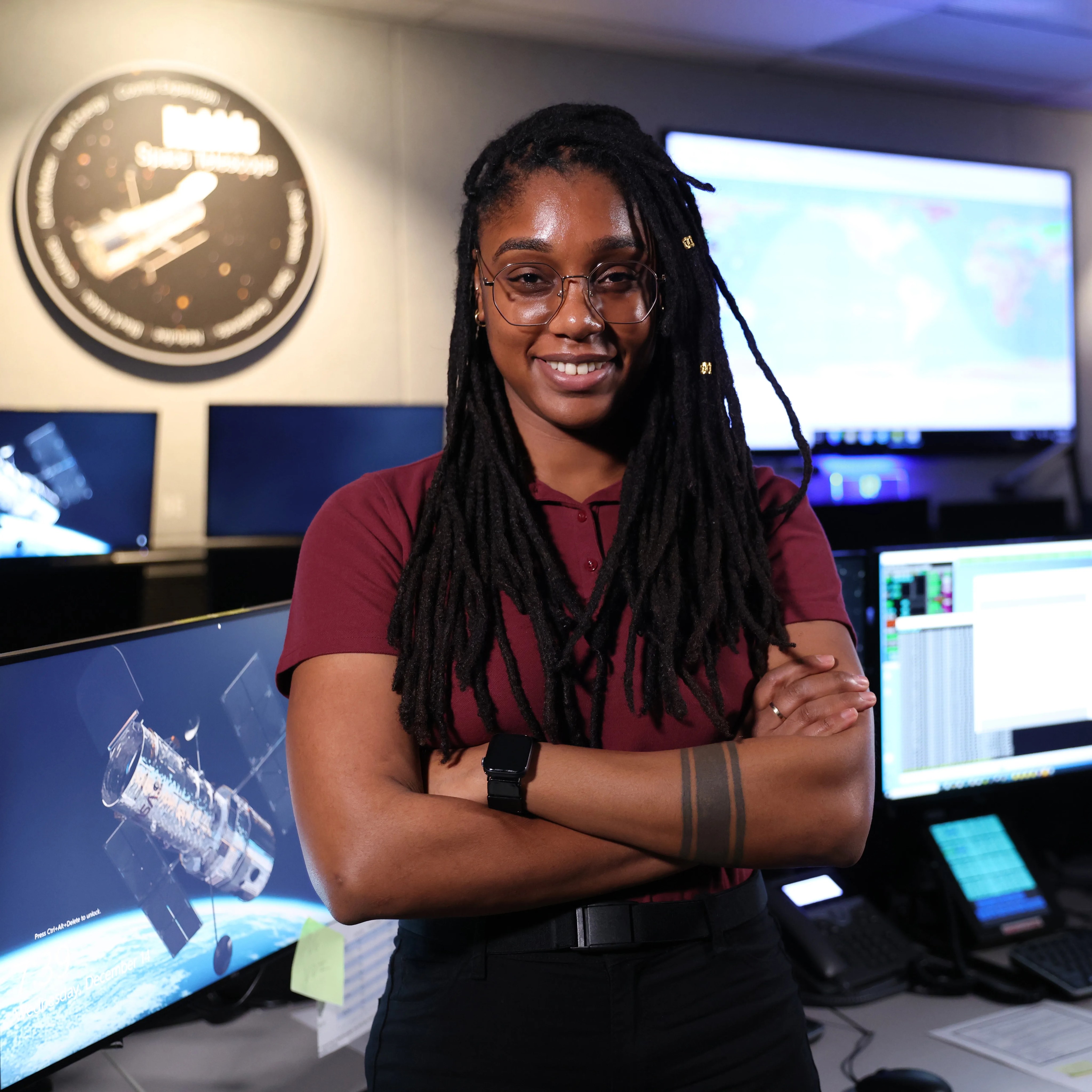 headshot of a woman standing in front of a desk with computer monitors on it