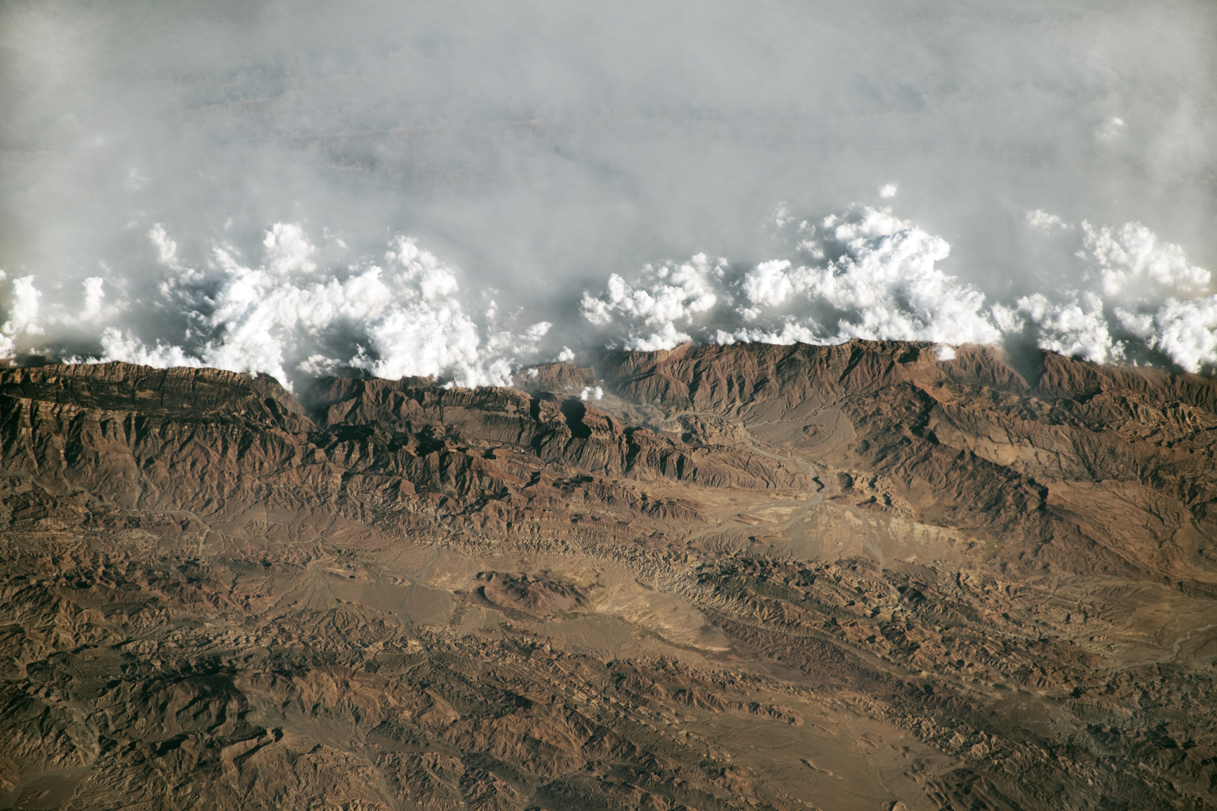 brown cragged barren landscape in the foreground immediately butted up against cumulous clouds with opaque haze beyond them