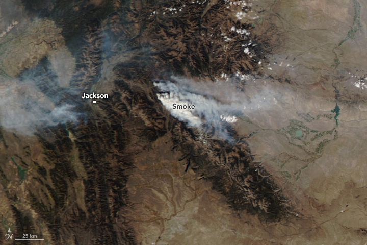 smoke streams from and obscures brown colored mountainous land in the center of the image.