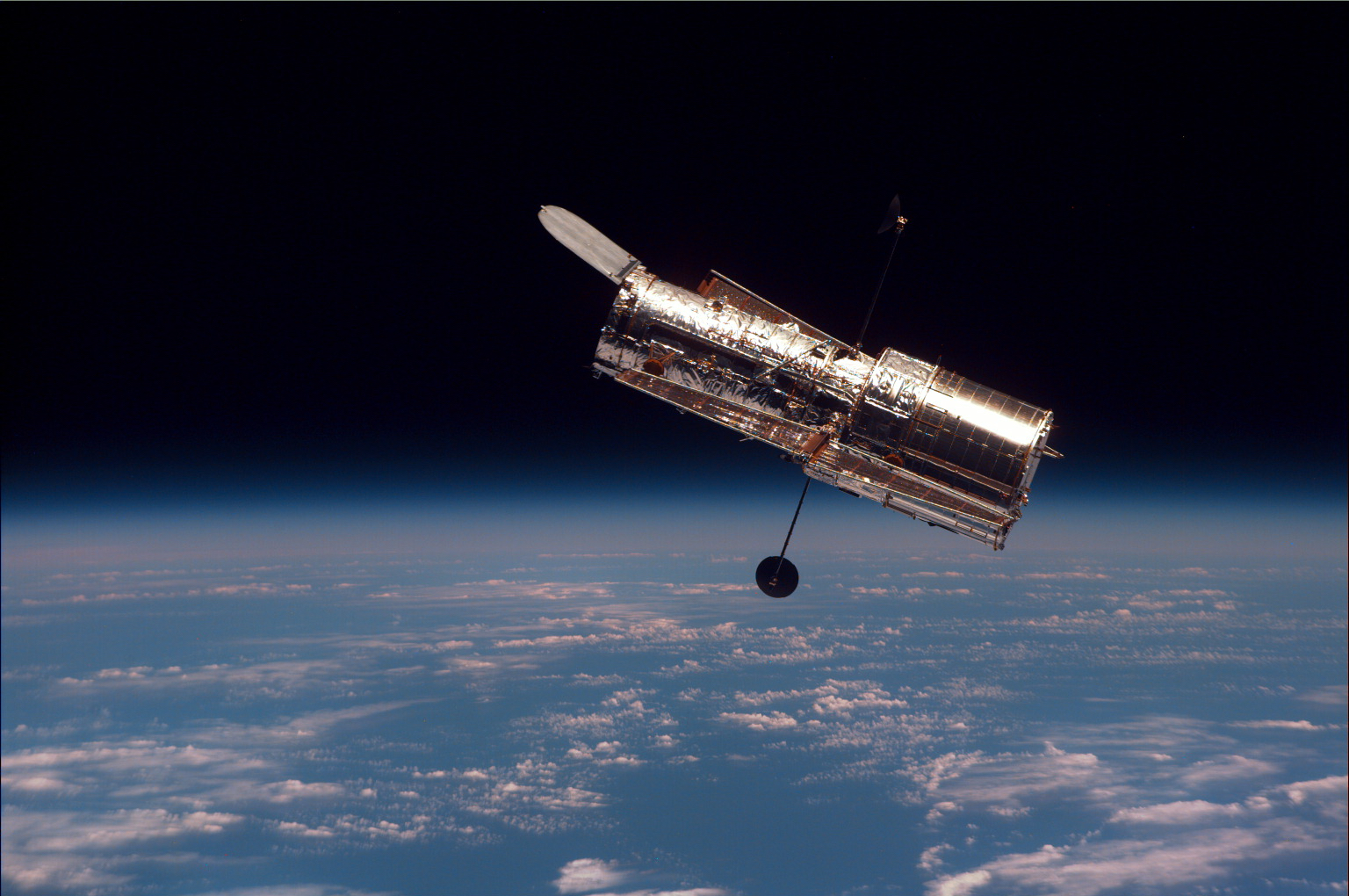 Hubble space telescope orbits above a blue Earth with white clouds.