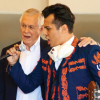 Carlos Alvarez sings into a microphone with a UTSA mariachi singer