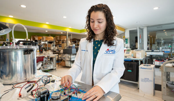 Isabella Cano adjusts electrical wires hooked to a device in a laboratory