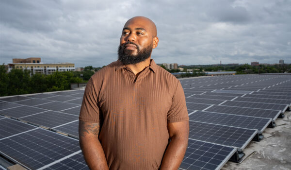 Jamal Hasty stands in front of solar panels on a rooftop at the Pearl