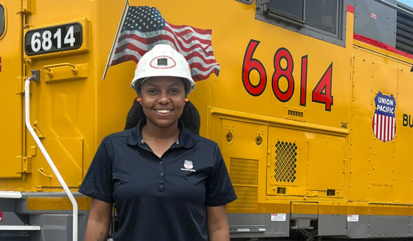 Taylor Richard poses in front of a large yellow locomotive