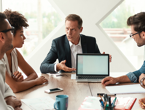 A group of professionals sitting at a table discussing something over a computer