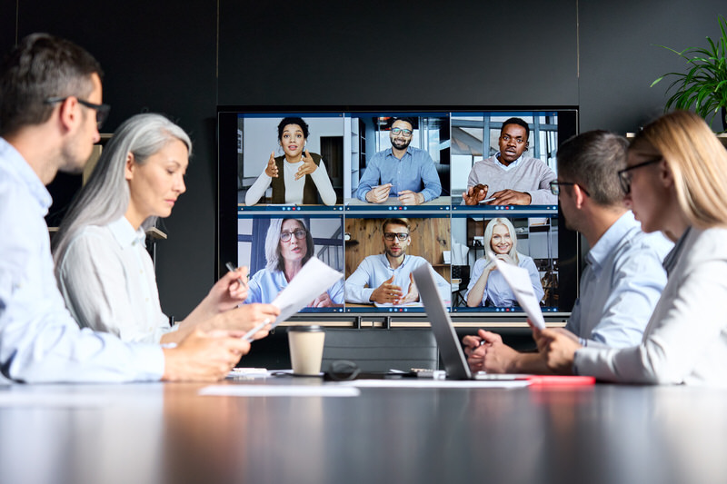 A group of professionals sitting in an office with a Zoom meeting going on