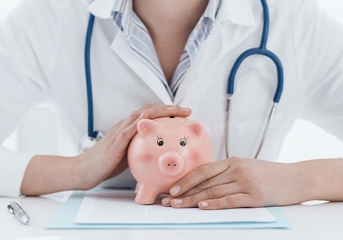 A doctor with her hands wrapped around a piggy bank.