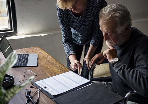 Elderly Man Sitting In Wheelchair Signing Papers