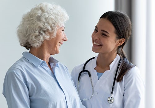 A doctor and an elderly woman smiling and looking at each other.