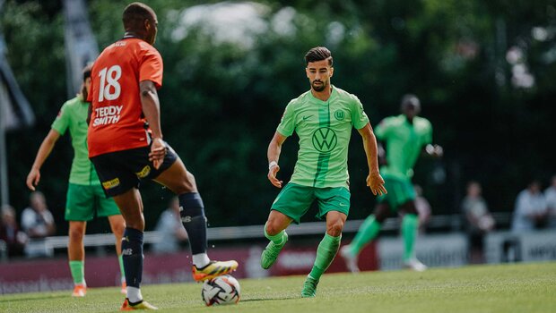 VfL Wolfsburg Spieler Mohamed Amoura hat den Gegner mit dem Ball am Fuß fest im Blick.