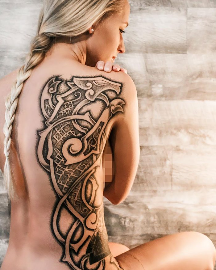 Woman with intricate Viking tattoo covering her back, featuring bold patterns and runes.