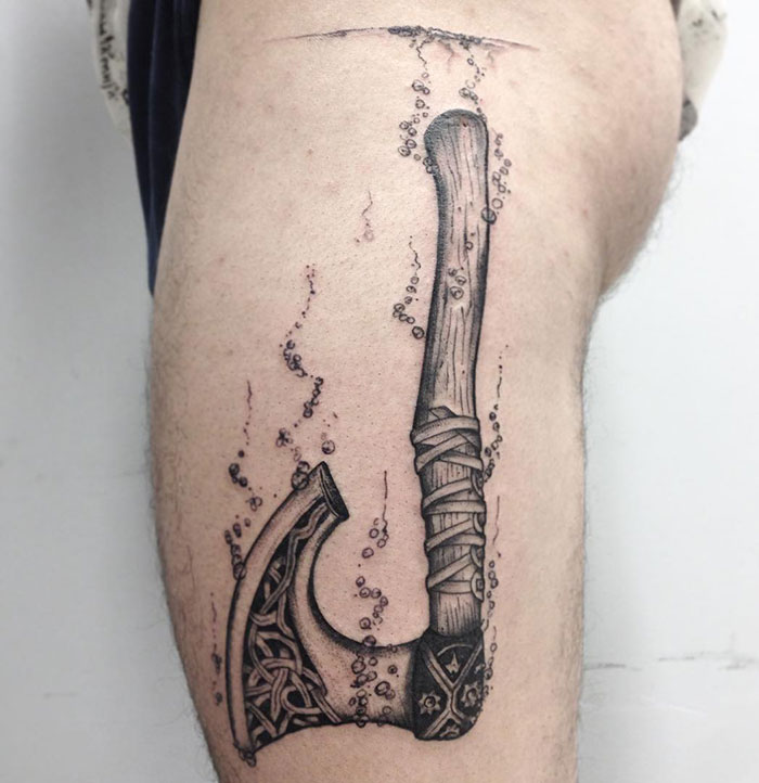 Viking tattoo depicting a detailed axe design on a person's leg.