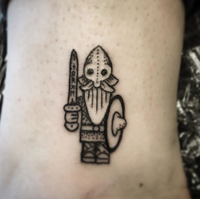 Cartoon style Viking tattoo featuring a bearded warrior with a sword and shield.