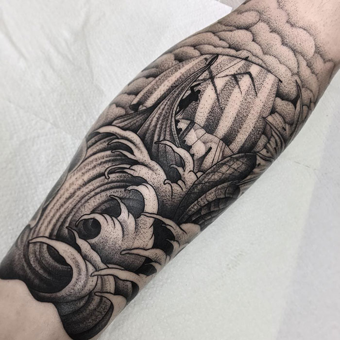 Black and gray Viking ship tattoo with stormy waves on forearm.