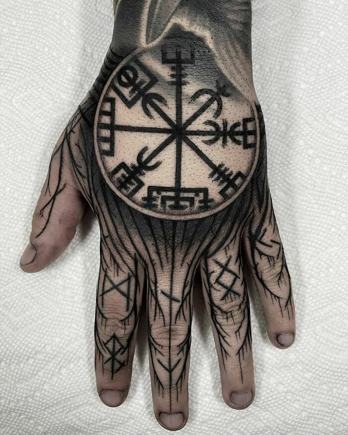 Hand with intricate Viking tattoo featuring runes and symbols, showcasing Norse design elements.