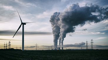 Single wind turbine, a coal burning power plant with pollution and electricity pylons in the background.