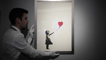 A staff member poses for photographs with a print of 'Girl with Balloon, 2004' by British street artist Banksy at Bonhams auction house in London, November 8, 2021