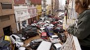 A woman looks out from her balcony as vehicles are trapped in the street during flooding in Valencia