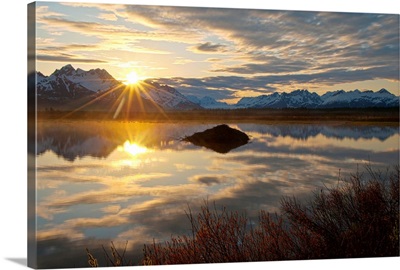 Sun rises over the Chugach Mountains with a pond and beaver lodge in the foreground