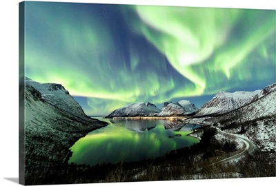 Northern lights and stars light up the snowy peaks reflected in the cold sea