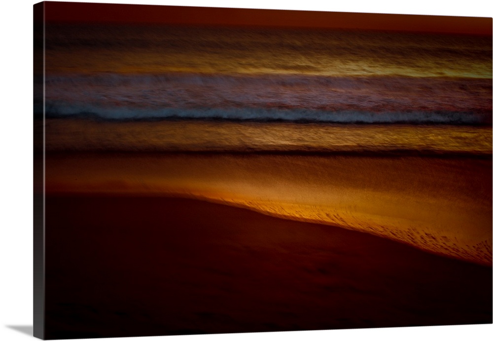 Golden lit photograph of ocean waves rolling on to the beach shore with a blurred look, created with a long exposure.