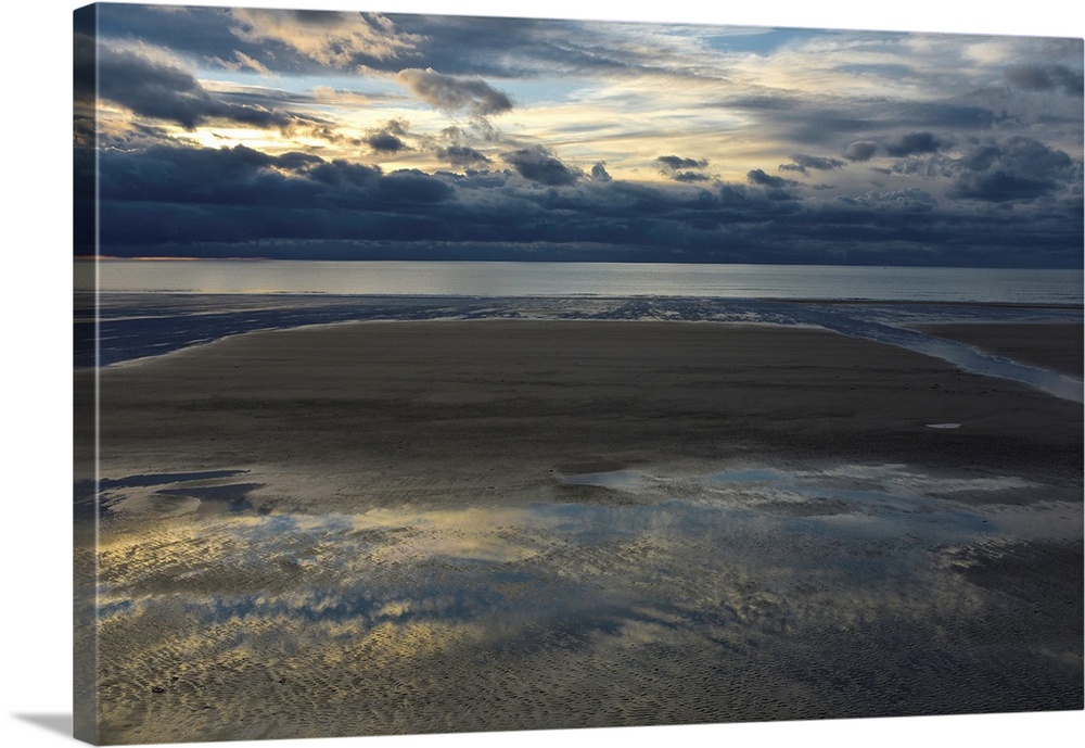 Landscape photograph of an empty beach on a cloudy day with the sky reflecting onto the puddles in the sand.